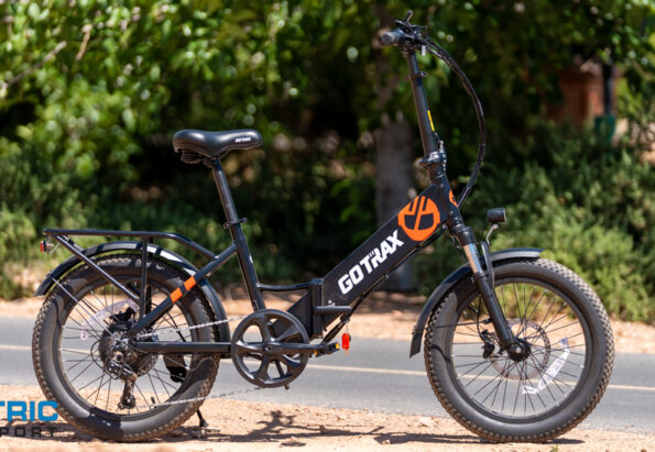 Black GOTRAX electric bike parked on a sunny roadside, side view with orange logo on the frame