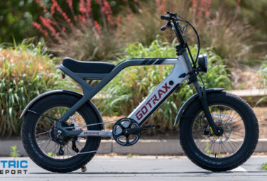 Side view of an electric fat-tire bike parked in a lot; gray frame, black components, and chunky tires.