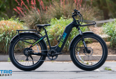 GOTRAX electric fat-tire bike parked in a paved lot with plants and a white fence in the background.
