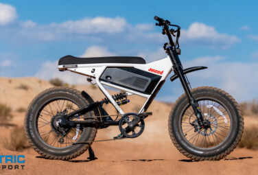 White Juiced electric fat-tire bike on sandy desert terrain under a blue sky; Electric Bike Report logo appears bottom-left.