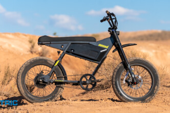 Juiced electric fat-tire bike on a sandy desert trail with a blue sky and sparse vegetation; logo visible on the frame.