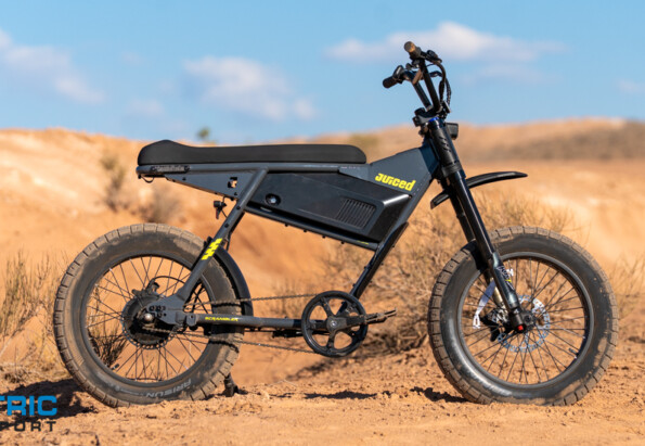 Juiced electric fat-tire bike on a sandy desert trail with a blue sky and sparse vegetation; logo visible on the frame.