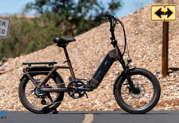 Electric bike with rear rack parked on a paved road beside a rocky slope; warning sign reads 'Do Not Enter When Flooded' and a yellow two‑way sign is in the background.