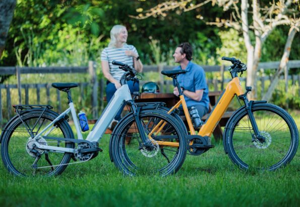 Two people chat at a wooden table in a park, with several colorful bicycles parked in front.