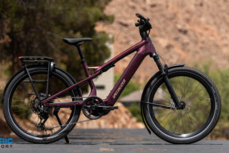 Specialized electric mountain bike in burgundy parked on a paved road with a rocky hillside in the background.