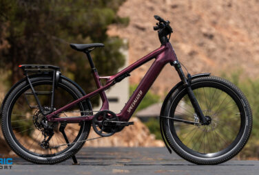 Specialized electric mountain bike in burgundy parked on a paved road with a rocky hillside in the background.
