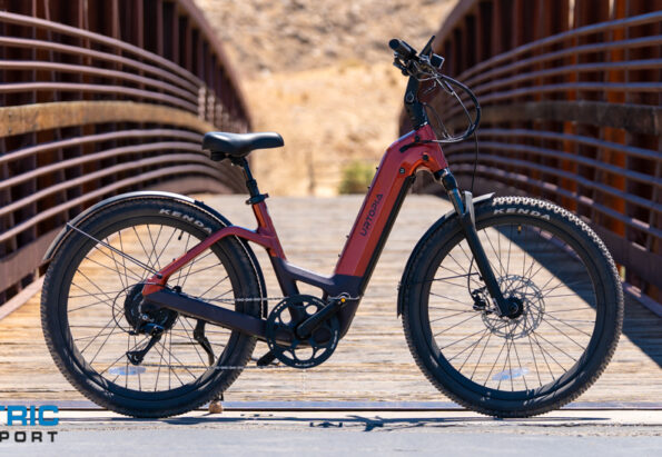 Electric cargo-style i.e. step-through electric bike parked on a wooden bridge with rust-colored rails, front and rear disc brakes visible, logo 'UTOPIA' on the frame, and 'Electric Bike Report' watermark bottom left.