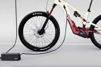 Electric mountain bike being charged, with a black charger and power cord on a light gray studio floor