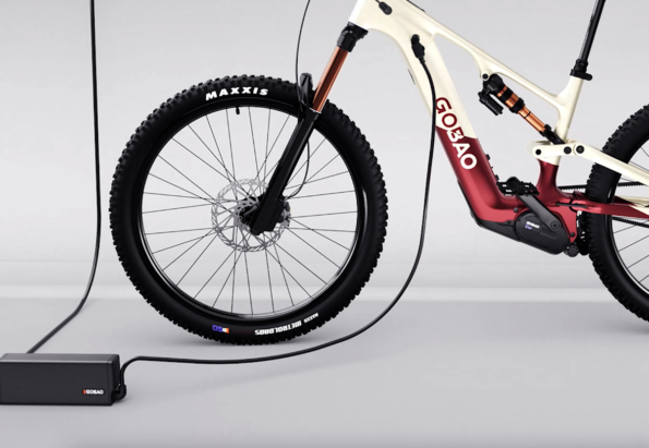 Electric mountain bike being charged, with a black charger and power cord on a light gray studio floor