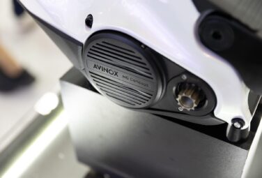 Close-up of a white motorcycle frame with a black round cover labeled 'AVINOX MG Concept'